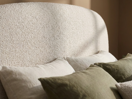 Detailfoto van het gestoffeerde bouclé hoofdbord van het Elena bed met sierkussens